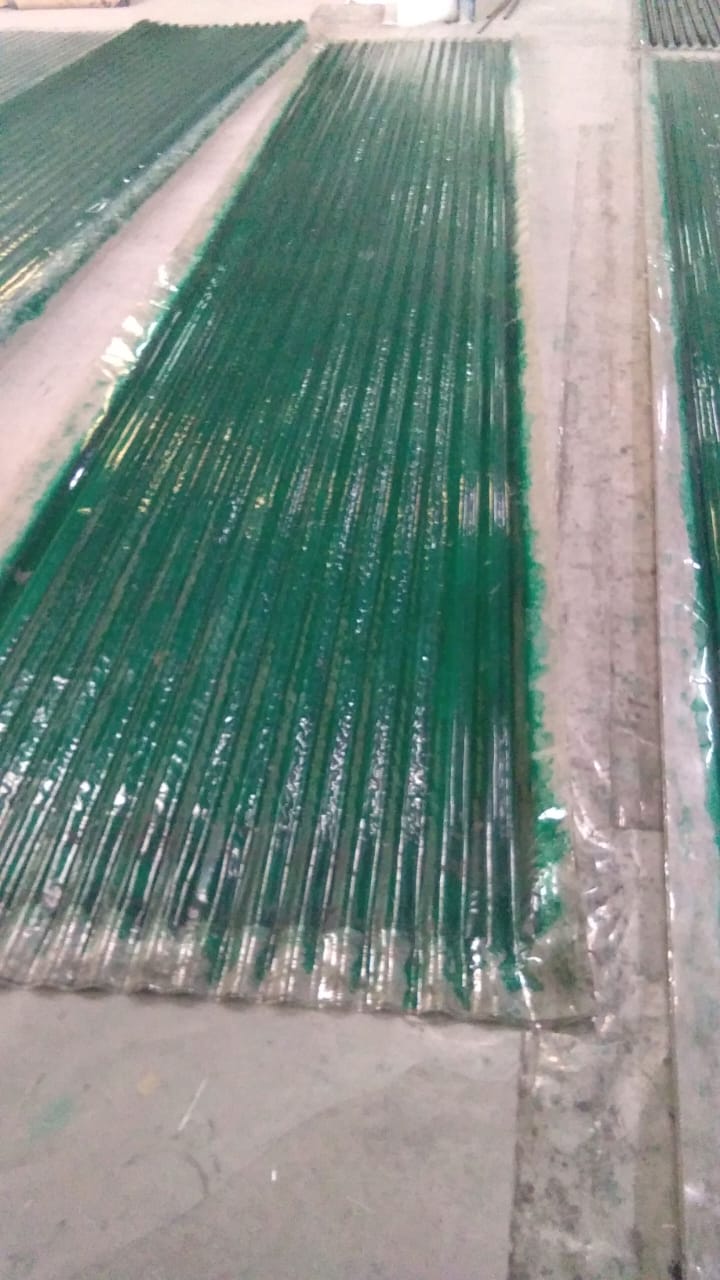 Green translucent FRP corrugated sheets stacked on floor, showing ribbed profile and glossy finish.
