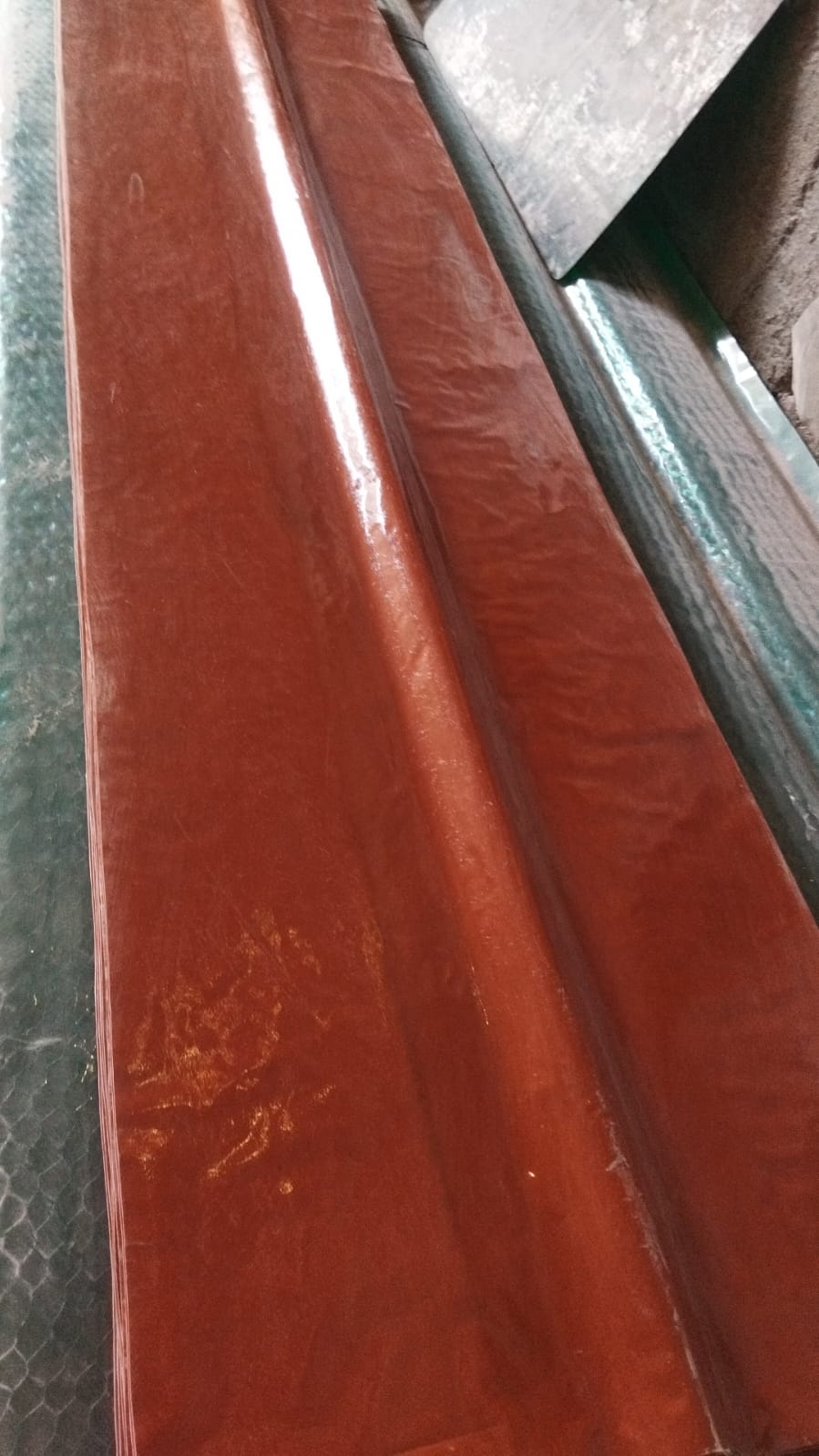 Stack of terracotta FRP ridge sheets on green corrugated base, showing ridge cap profile and alignment.