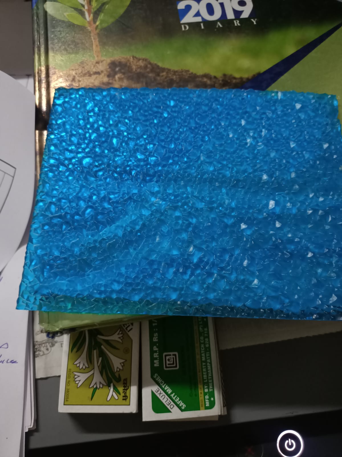 Vibrant blue polycarbonate diamond sheet sample with crystalline diamond texture on desk.