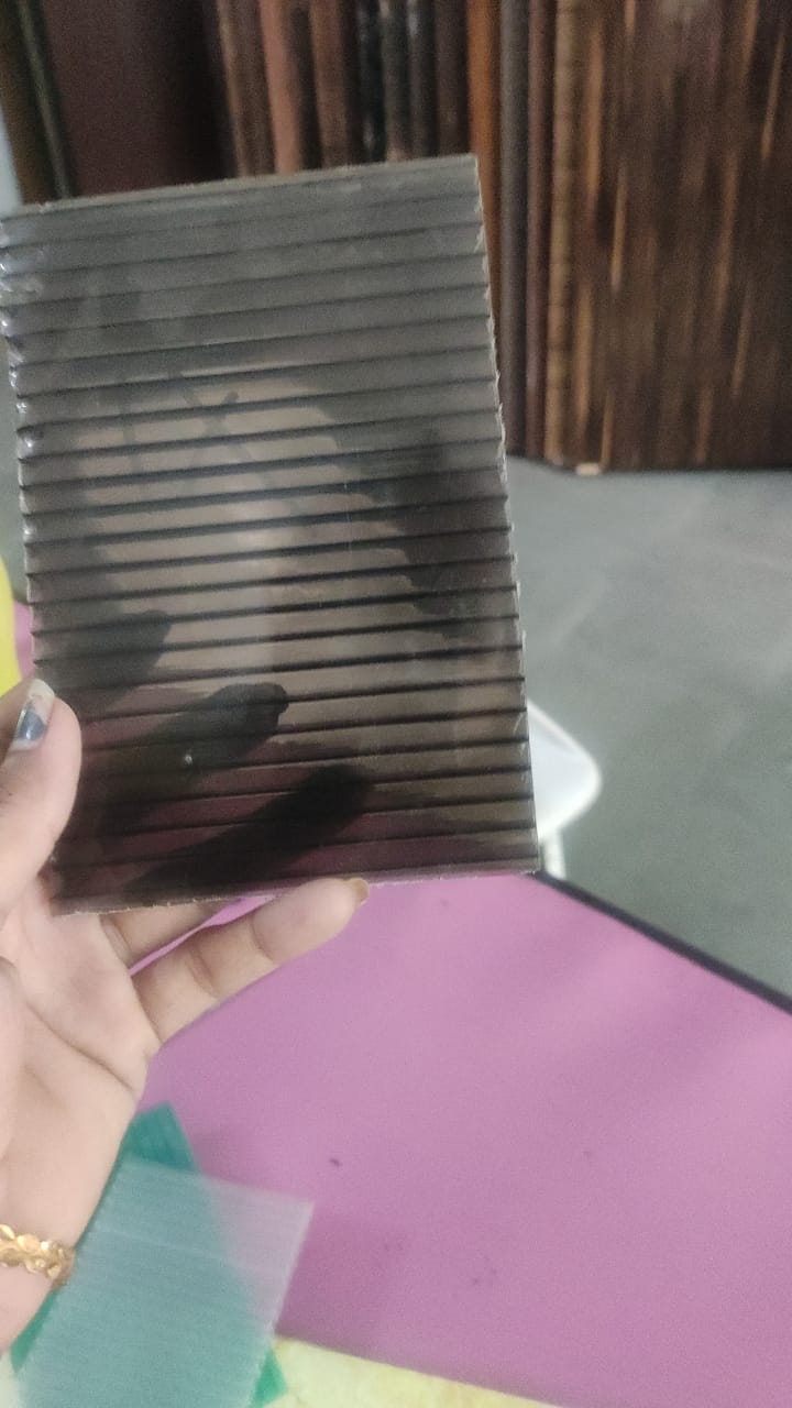 Hand-held sample of dark translucent multiwall polycarbonate sheet showing parallel channels.